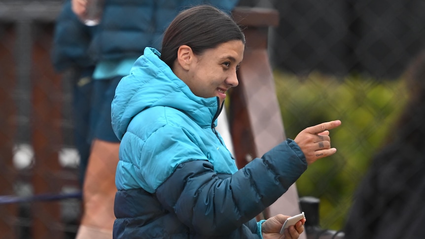 Sam Kerr smile and points, wearing a Matildas-branded puffer jacket