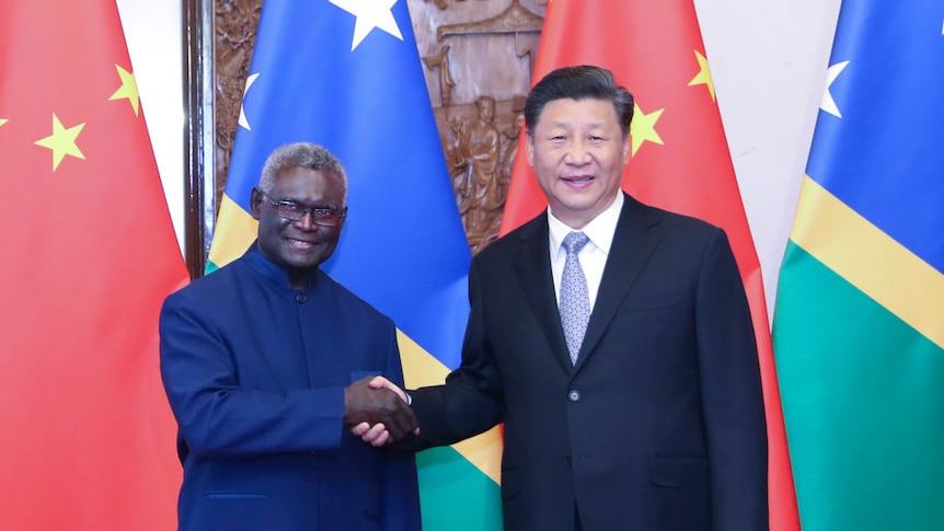 Chinese President Xi Jinping shakes hands with Solomon Islands' Prime Minister Manasseh Sogavare, in front of their flags