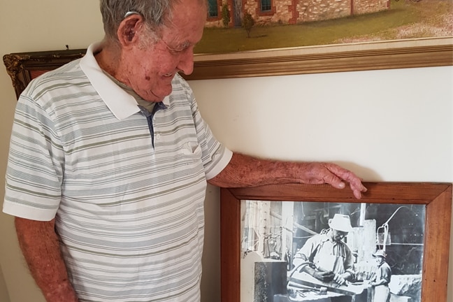 Elderly man smiles at a photo frame with black and white image of his father. 