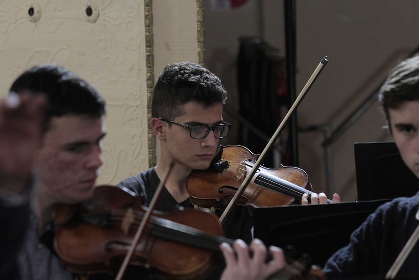 Aboud Kaplo sitting amongst other orchestra members of the Western Sydney Youth Orchestra during a rehearsal