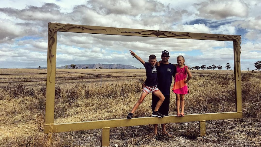 A man and two children inside a huge picture frame near Horsham