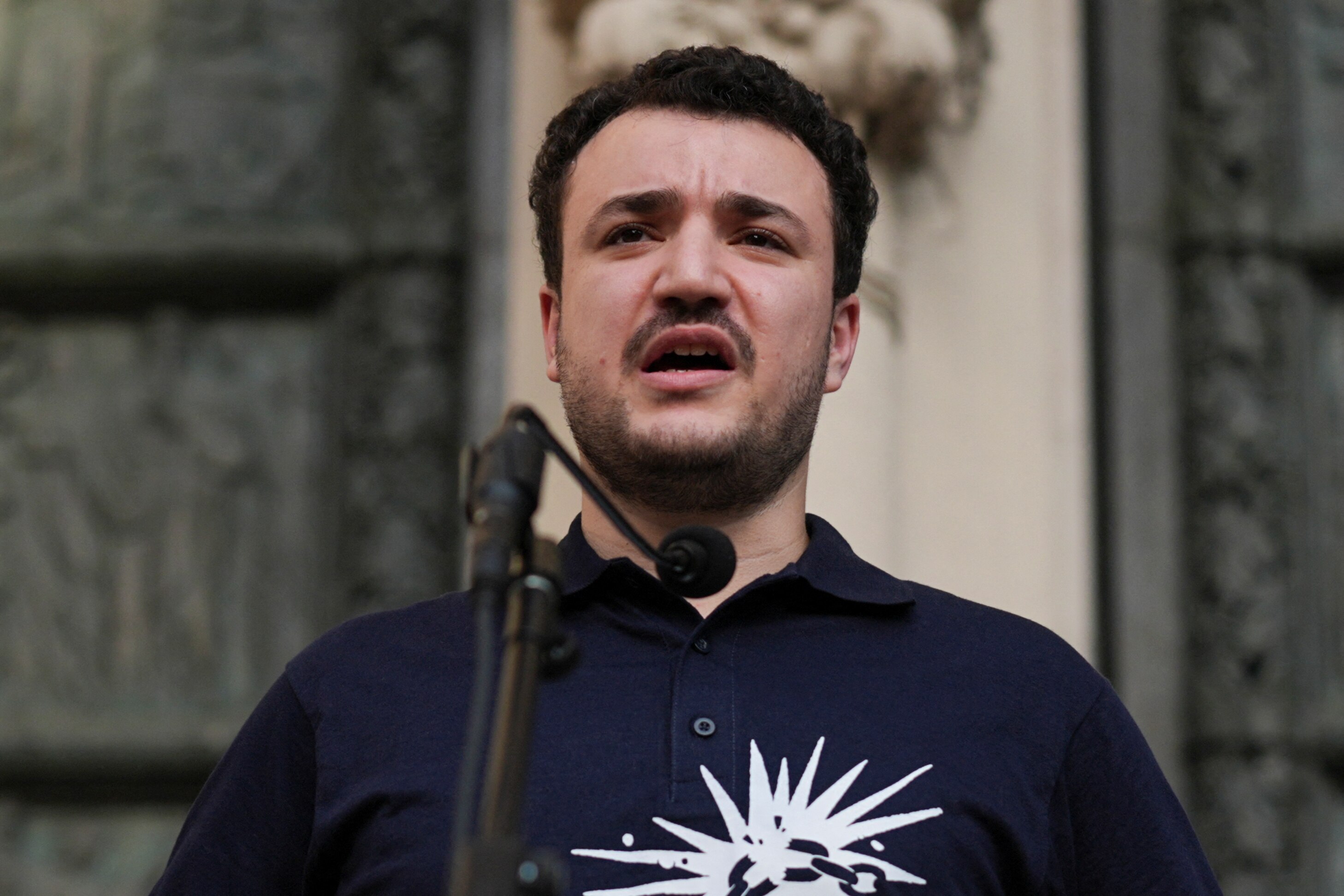 A man in a navy polo shirt speaks into a microphone