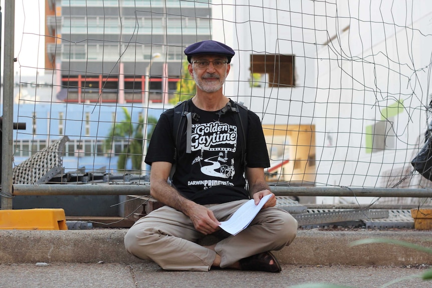 A man sits next to a wire fence.