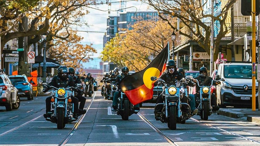 Motorbikes, one carrying the Aboriginal flag ride ahead of a black hearse.