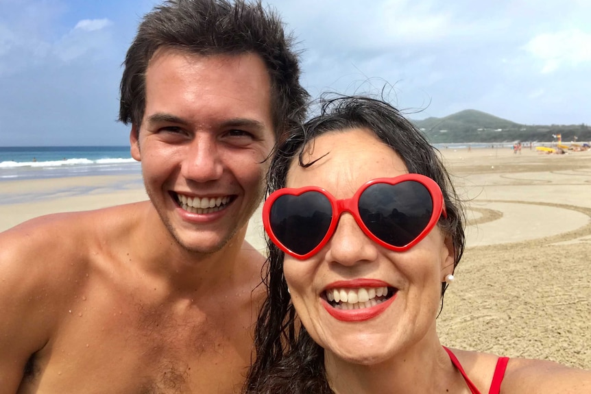 A man and woman smile on a beach.