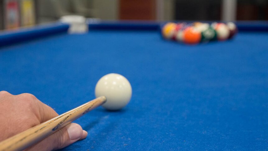 Close up of hand and cue lining up break shot on blue-covered pool table.