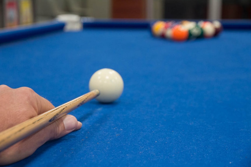 Close up of hand and cue lining up break shot on blue-covered pool table.