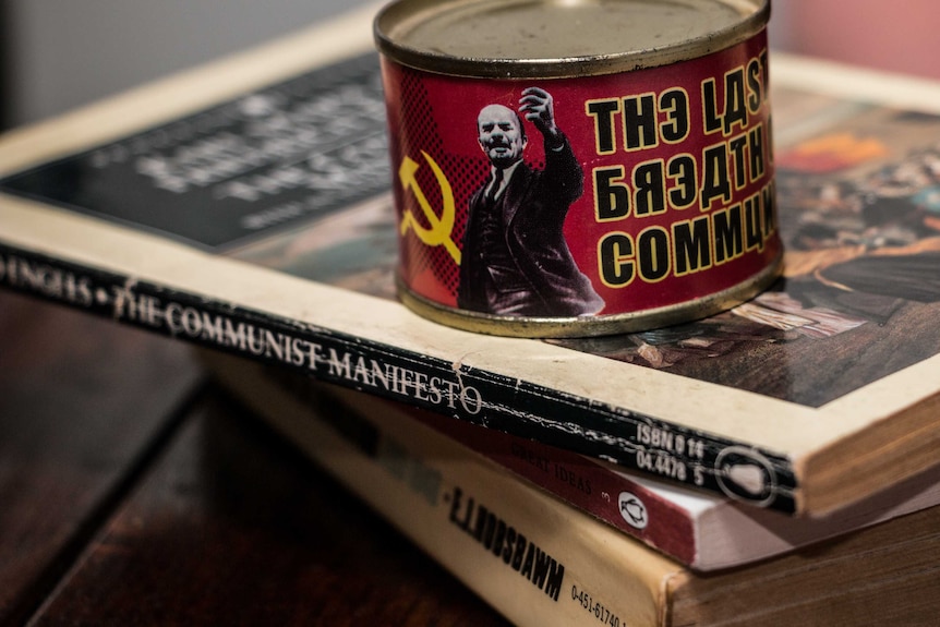 An ashtray with Vladimir Lenin and a hammer and sickle on it sits on top of The Communist Manifesto by Karl Marx