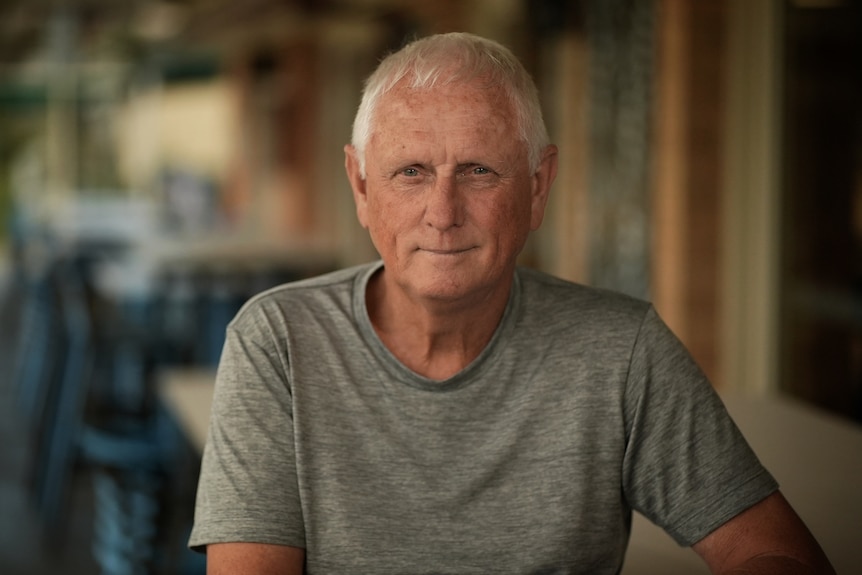 A man in a grey shirt smiles at camera.