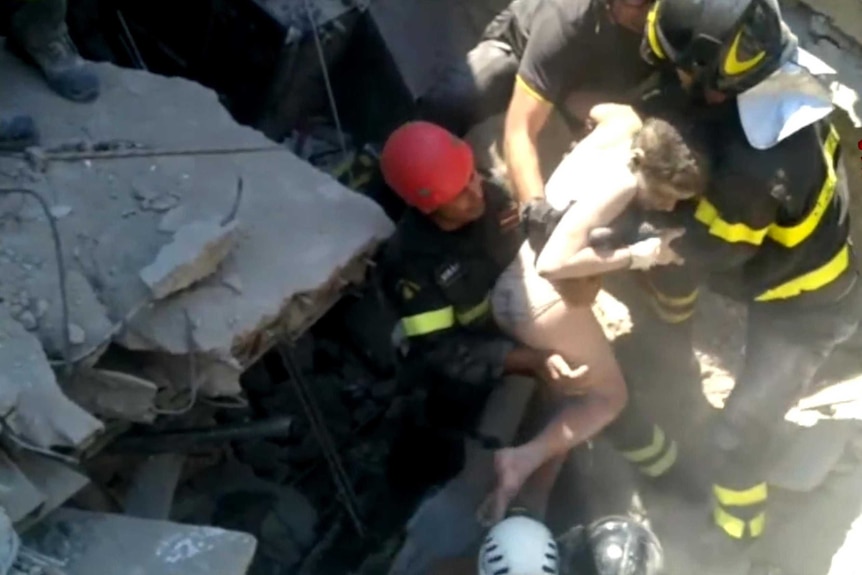 A young boy wearing only his underwear is pulled from rubble by firefighters.