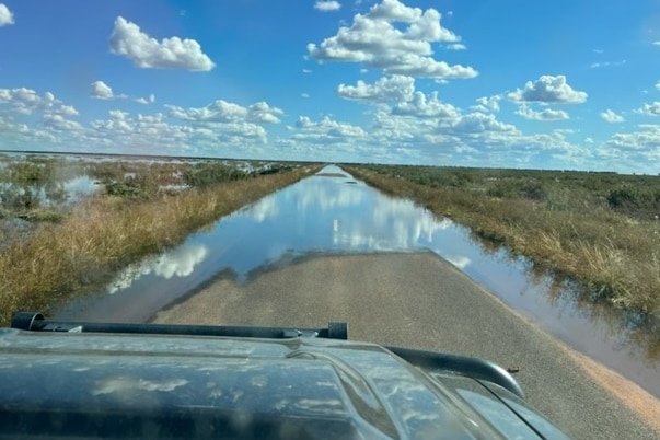 A flooded road with the bonnet or a car in the foreground.