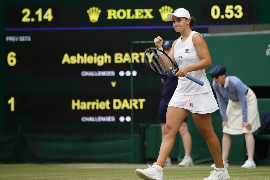 A female tennis player walks as she raises her right fist with a scoreboard in the background.