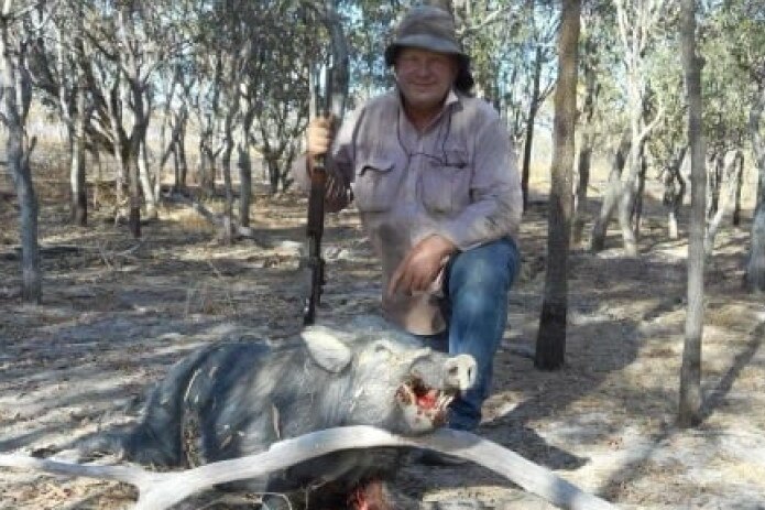 Shane Knuth with a rifle in his hand standing over a dead pig