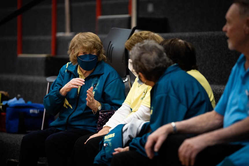 Group of older women with masks on talking to each other in a gymnasium.