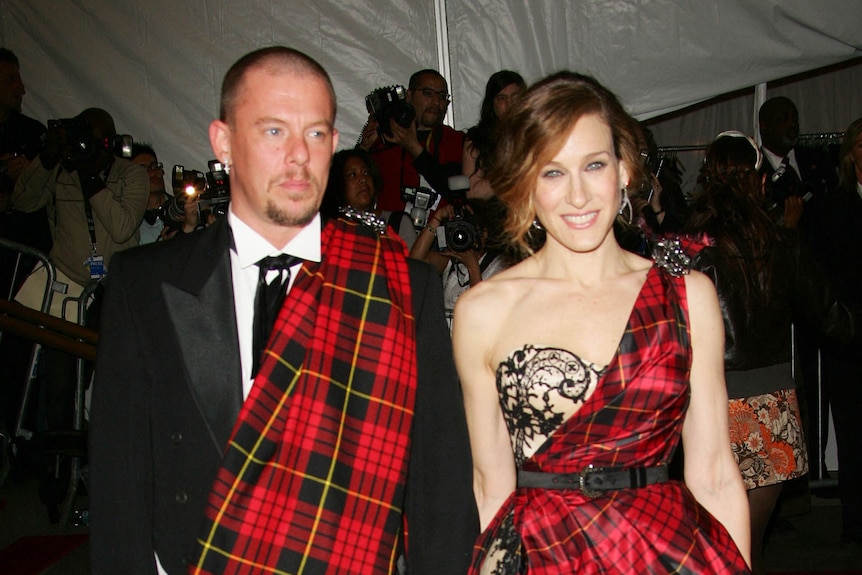 A man wearing a suit and tartan sash stands with a Sarah Jessica Parker wearing a tartan dress.