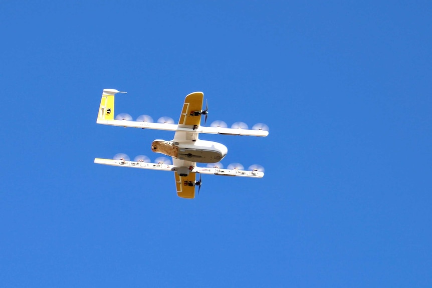 A drone, which looks like a small plane, flies through a blue sky.