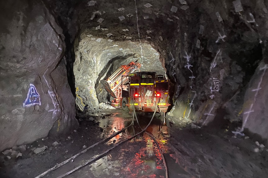 Large mining machine sits in dark underground tunnel, lighting up centre as it drills through rock