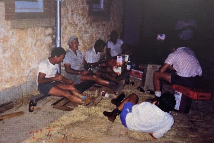Men wearing shorts and boots sit on an incomplete floor, having a break as they build.
