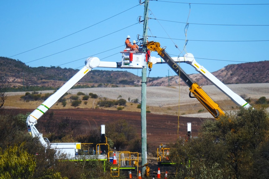 Two men in high vis on cranes repairing a power pole