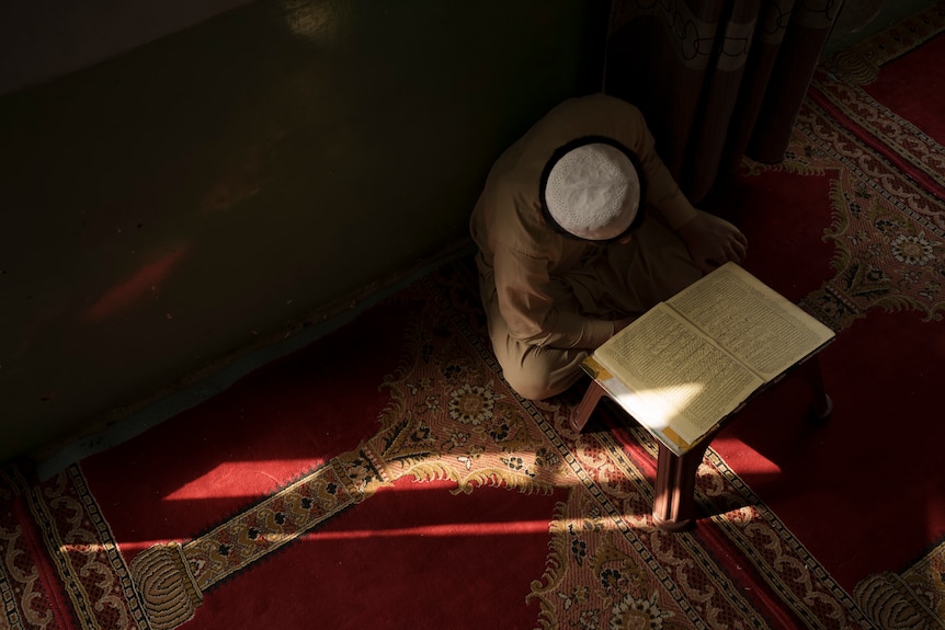 A top-view of a boy in a skullcap reading the Quran in a Kabul madrassa.