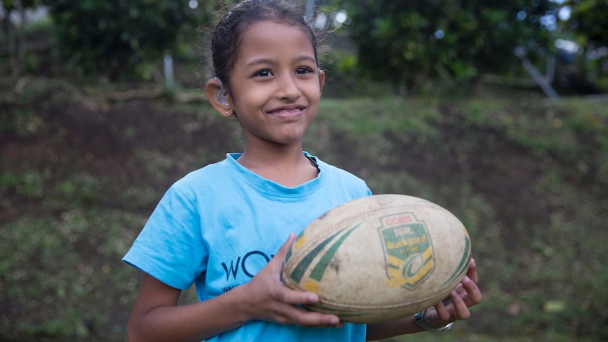 A hearing impaired Fijian girl smiles while holding a ball.