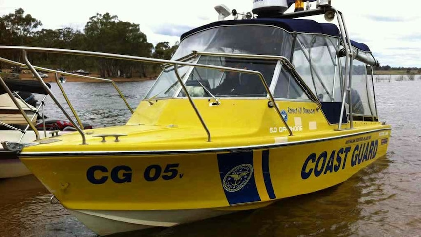 A thirty year old boat sits in the shallow waters of Lake Eppalock, it is bright yellow and has Coast Guard written on the side