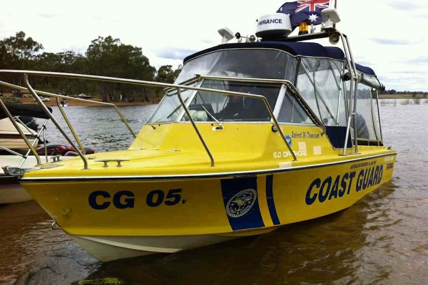 A thirty year old boat sits in the shallow waters of Lake Eppalock, it is bright yellow and has Coast Guard written on the side