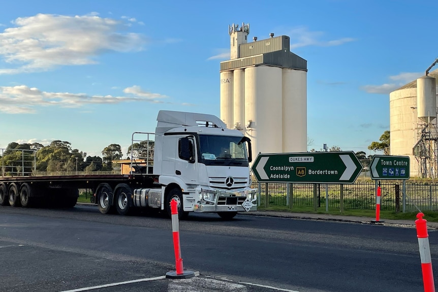A large truck drives past silos and a road direction sign