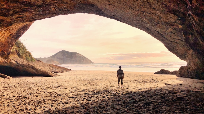 A male figure standing in a cave, looking out at the ocean and horizon