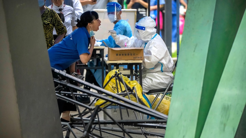 A worker wearing a protective suit swabs a woman's throat