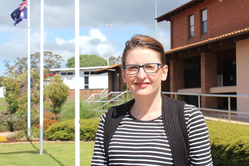 A woman with short brown hair wearing glasses and a top with horizontal stripes stands outside an office building