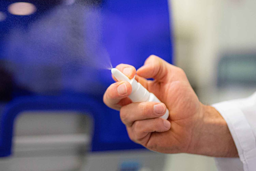 A close up of a person's hand squeezing a nasal spray bottle, with the contents spraying into the air.