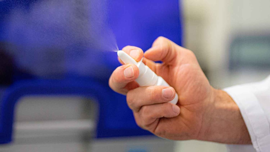 A close up of a person's hand squeezing a nasal spray bottle, with the contents spraying into the air.