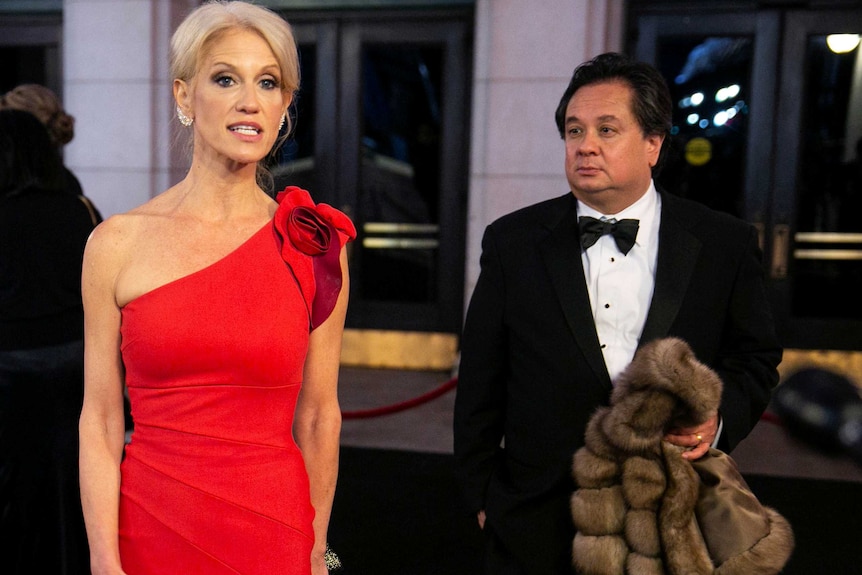 A woman in a red dress poses for the camera while a man holds her fur coat