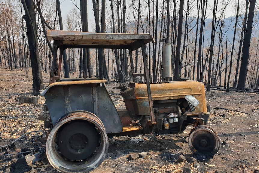 a burnt tracker in front of trees burnt by a fire