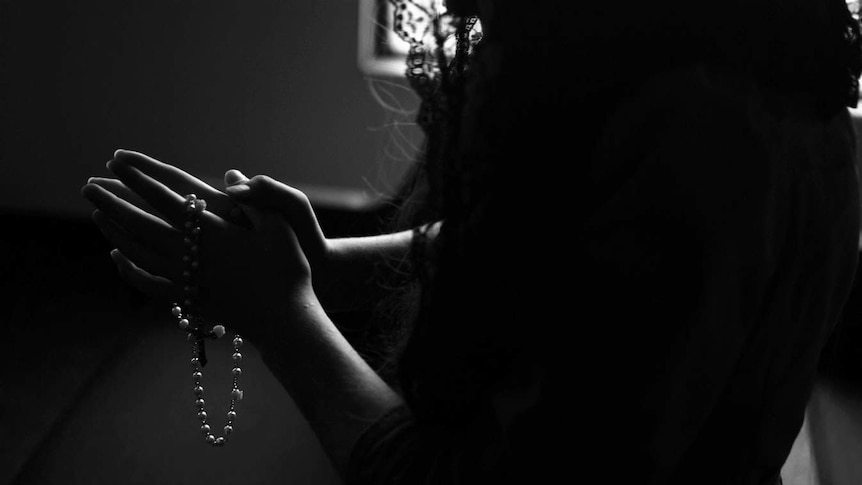 A woman prays the rosary, her head is covered, the picture is black and white.