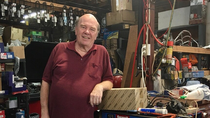 A man standing in a mechanics workshop surrounded by tools and spare parts