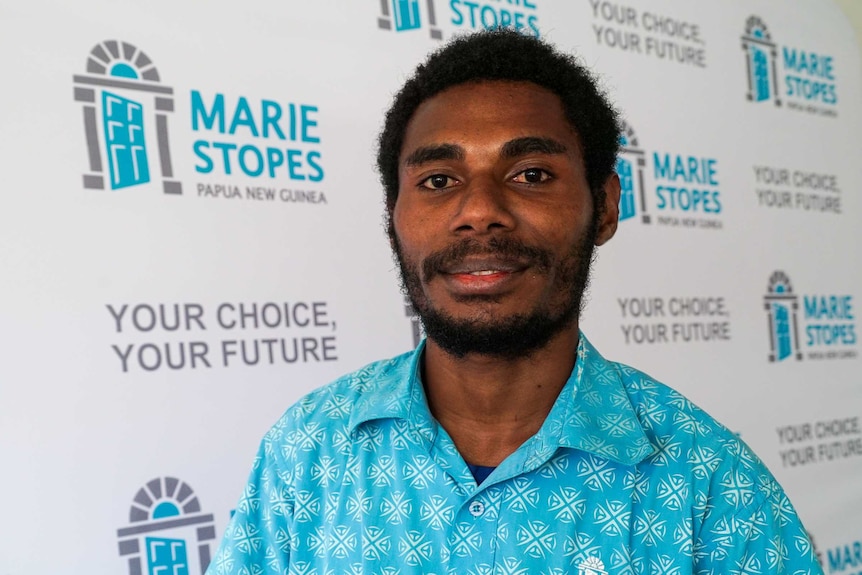 A man in a blue shirt standing in front of a Marie Stopes sign
