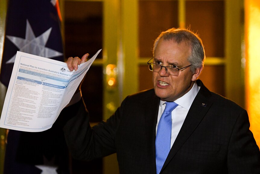 Scott Morrison holds up a document during a night-time press conference at the Lodge