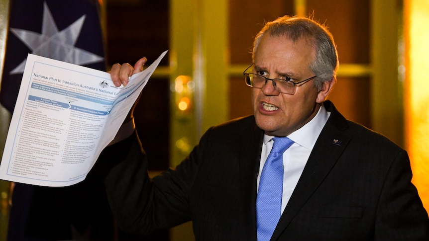 Scott Morrison holds up a document during a night-time press conference at the Lodge