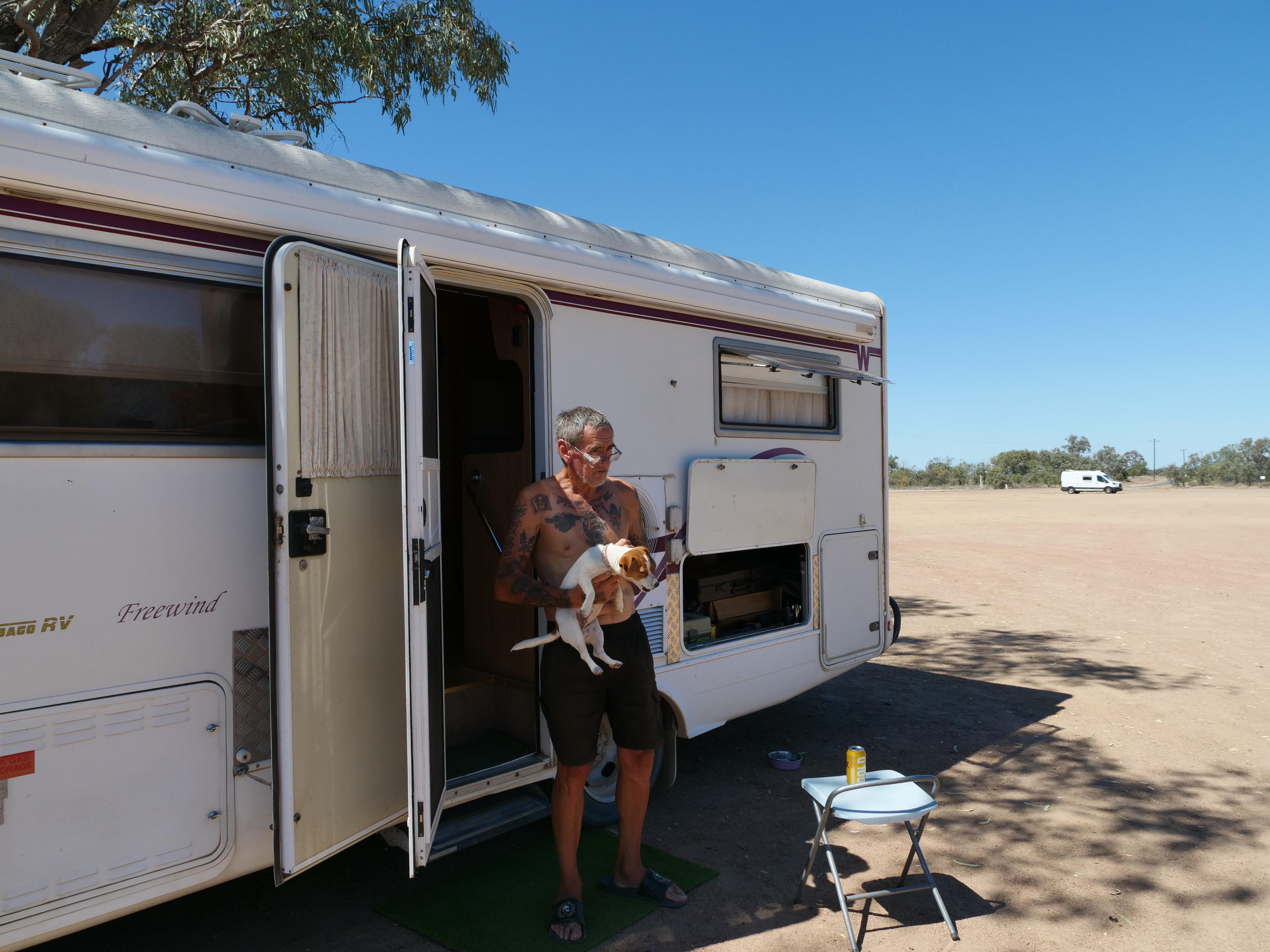 A man stands with his caravan and a dog.
