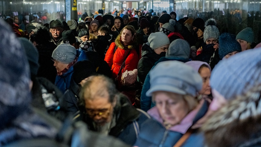 A woman stands in the light among a crowded tunnel. 