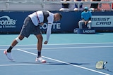 Nick Kyrgios is hunched over looking at his racquet, which he smahes on the tennis court.