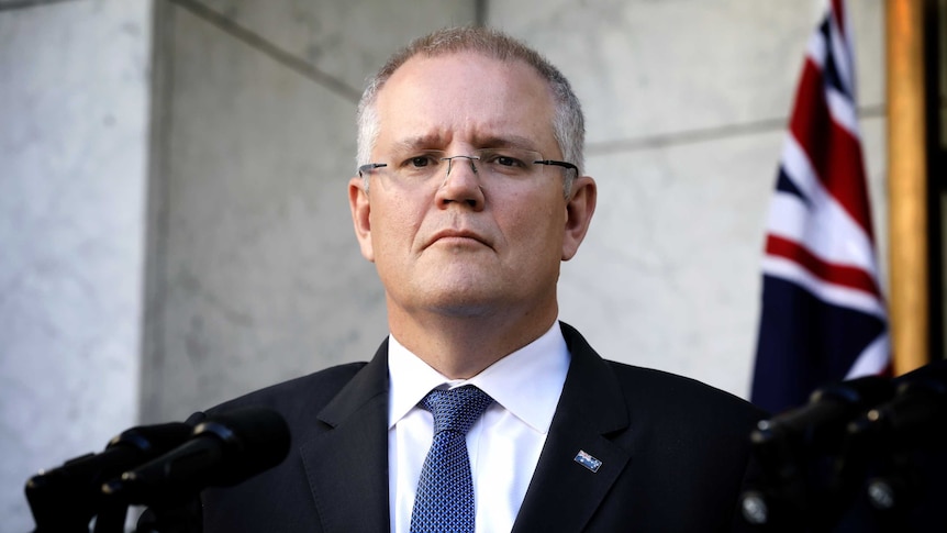 Scott Morrison stands in front of microphones looking terse