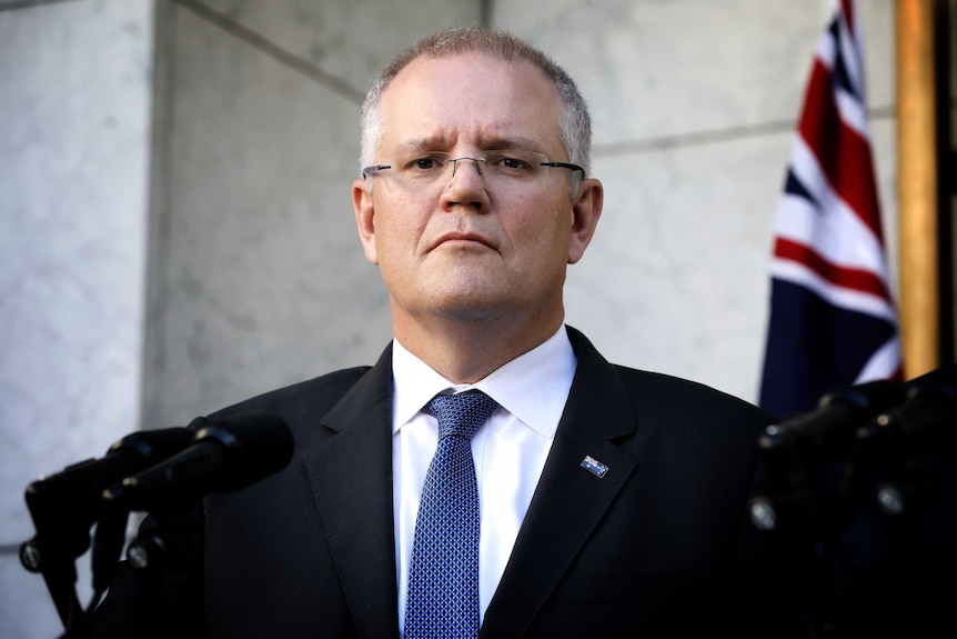 Scott Morrison stands in front of microphones looking terse