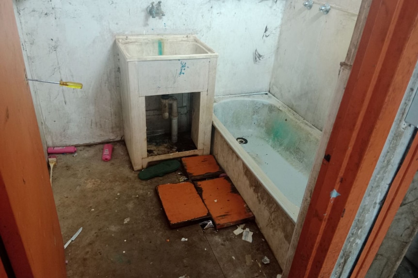 A bathroom with mouldy walls, missing floors and fixtures