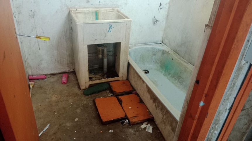 A bathroom with mouldy walls, missing floors and fixtures