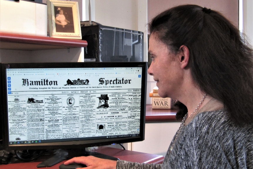 A dark-haired woman reads an old online newspaper.