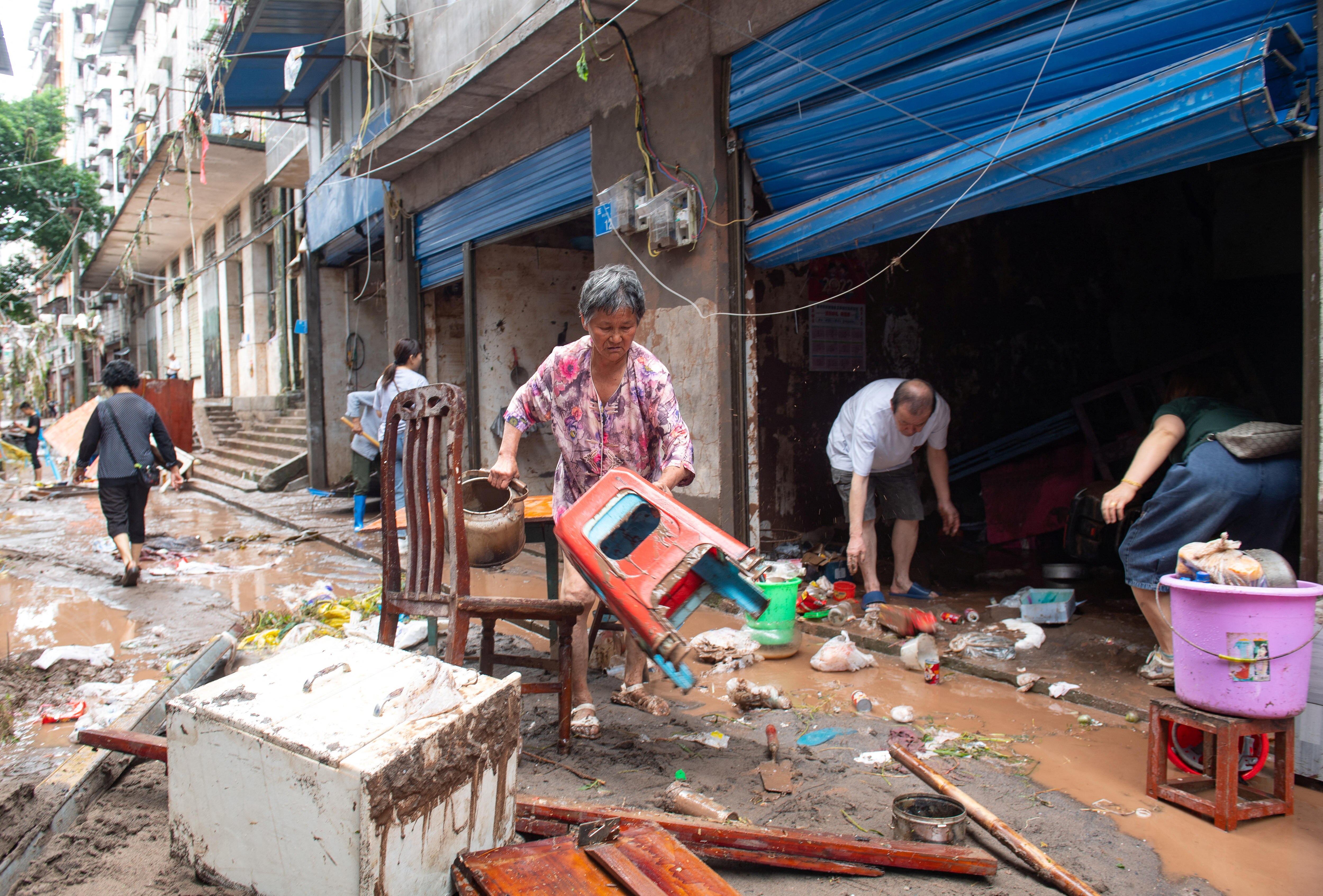 People are picking up items of furniture covered in mud on a driveway.