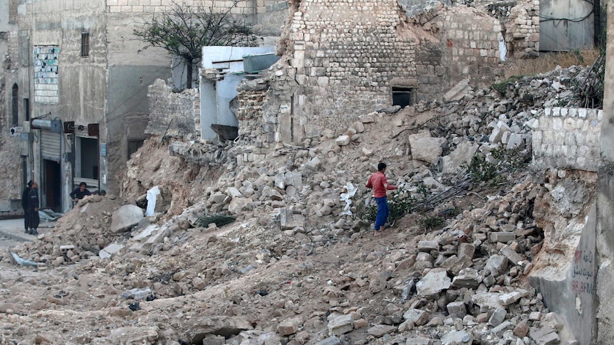 A civilian collects tree branches amid the rubble of a damaged site in the rebel-held besieged Qadi Askar neighbourhood of Aleppo, Syria